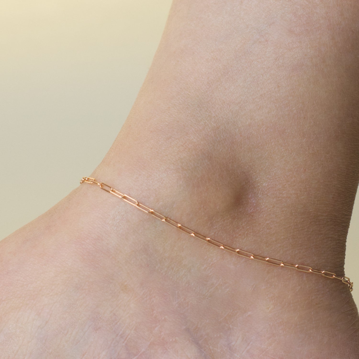 Woman wearing a 14K rose gold fill paperclip chain anklet with a minimalist style (small) link size